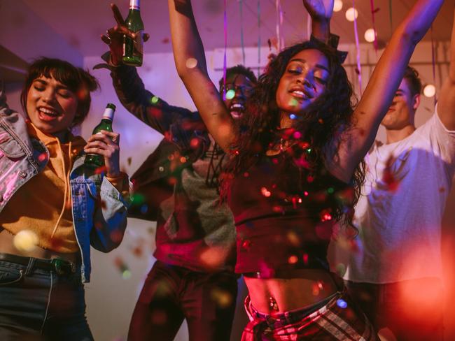 Young men and women having fun at a colorful house party with confetti all around. Friends dancing and celebrating holding drinks at a house party.