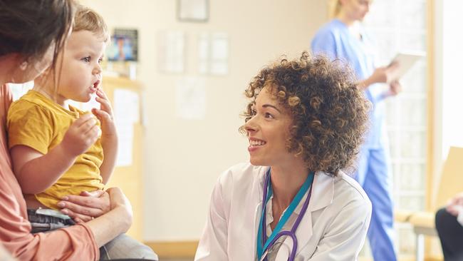 A young family sits talking to the doctor. The toddler is sat on his motherâ€™s knee as the doctor kneels down to talk to him