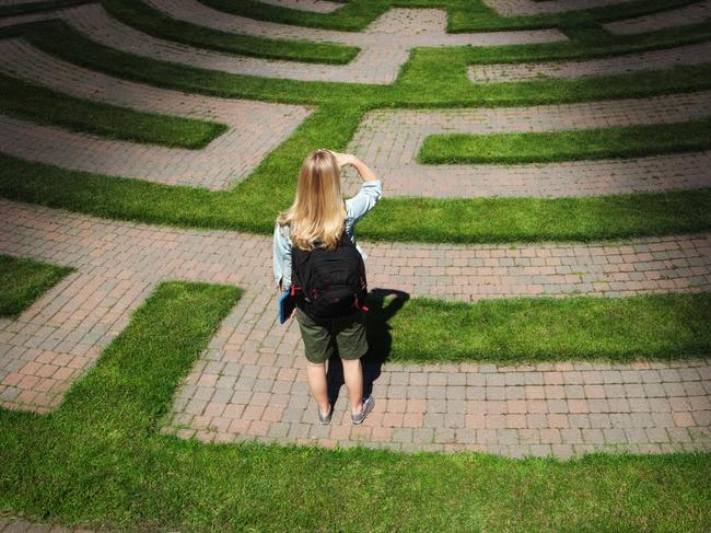 Predictions. A woman teenager student stands looking through the puzzling maze of schooling and the education system, forecasting the way forward and searching for the path to her goal. Concept of student facing uncertainty to their education, life and future career.