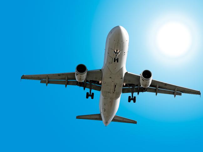 A jet aircraft landing under a sunny blue sky.