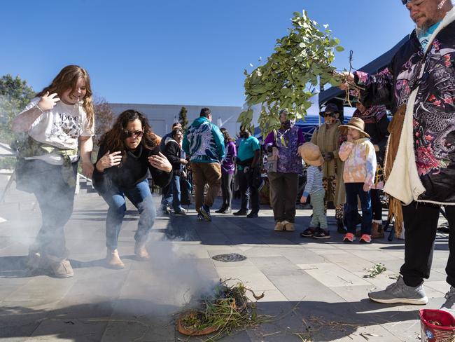 Grace Anstee (left) and mum Merinda Thompson let the smoke waft over them at a Smoking Ceremony conducted by Jarowair Wakka Wakka man Conrad Bauwens at the NAIDOC arts and craft market at Grand Central, Saturday, July 9, 2022. Picture: Kevin Farmer