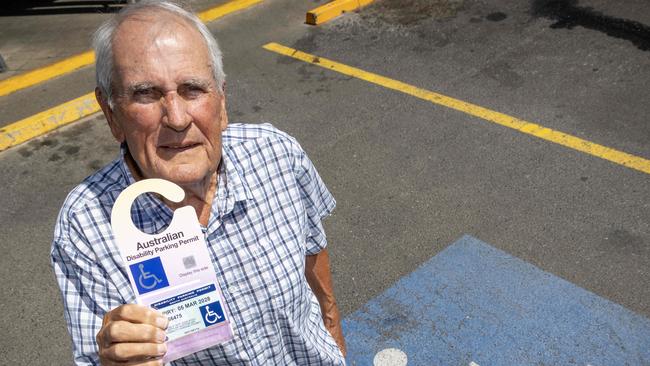 February 11, 2025:  John Houlahan accidentally parked in a disabled spot without his disability parking permit. He later showed council the permit, but they're insisting the 80+ year old jumps through hoops and red tape to waive the fee. Picture of John holding his disabled permit, outside a disabled parking spot. Picture: Kelly Barnes