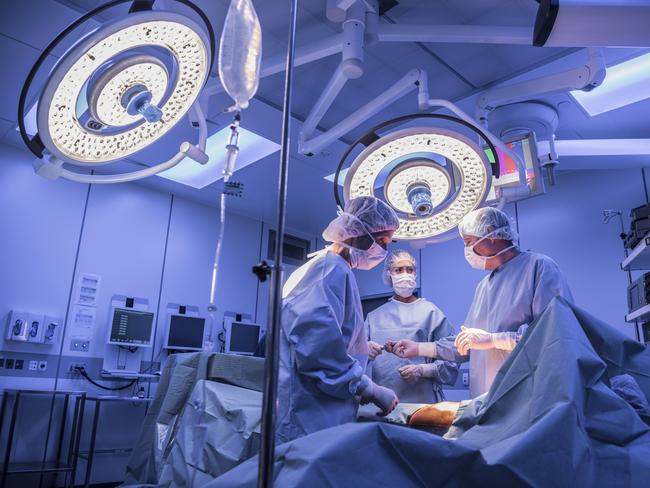 Doctors wearing surgical masks and gowns performing an operation on patient in hospital operating theater.