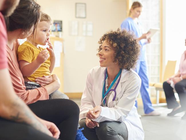 A young family sits talking to the doctor. The toddler is sat on his motherâ€™s knee as the doctor kneels down to talk to him