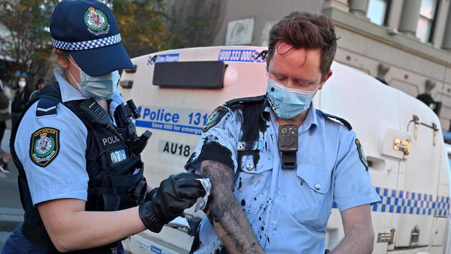 A police officer wipes away the paint thrown by a protester on her colleague in Sydney. Picture: Steven Saphore/AFP