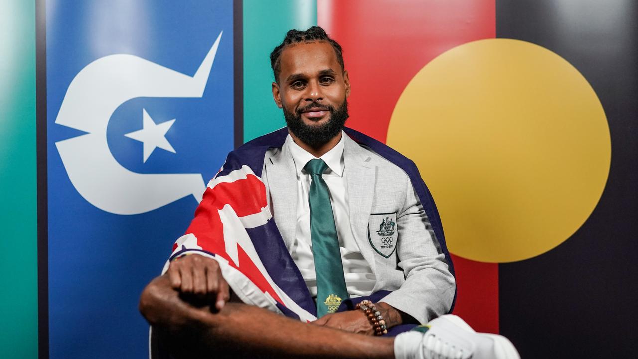 Joint Australian flag bearer for the Tokyo Games Patty Mills poses in front of the Torres Strait Islander and Aboriginal flags, with the Australian flag draped over his shoulders. Picture: Australian Olympic Committee/Getty Images