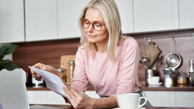 SENIOR/PENSIONER/MATURE/ELDERLY/OVER 65/GRANDPARENT/RETIREE/SUPERANNUATION. Picture: istock Middle aged older woman housewife reading paper letter or bill sitting in kitchen at home office, checking financial taxes fees, reviewing bank account loan rates information, medical insurance cost.