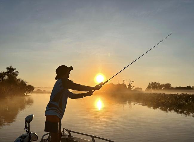 First light, first catch: A fisherman casts off into the calm waters of Corroboree Billabong at sunrise. Picture: Sam McManus