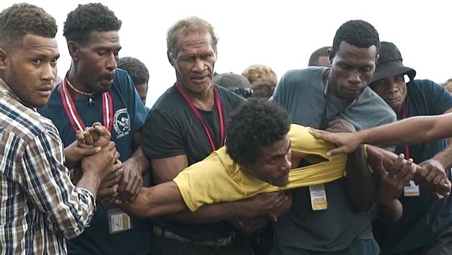 Solomon Islands security officials restrain a man who allegedly attacked a Japanese sailor with scissors during a World War II memorial ceremony. Picture: AFP