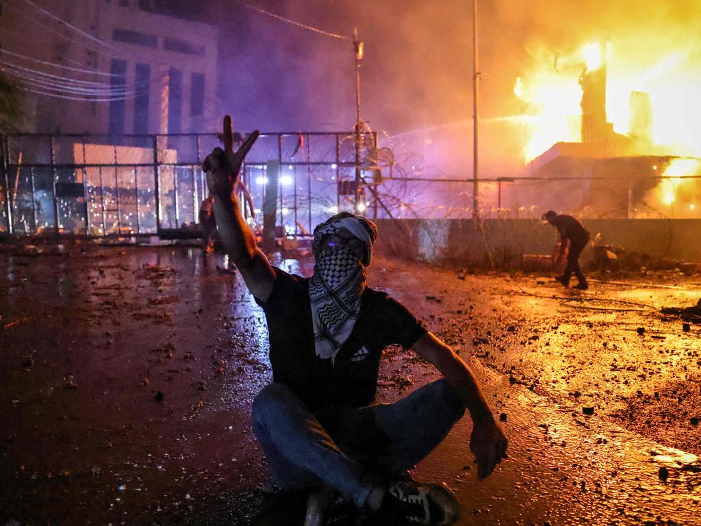 A Lebanese protester flashes the V for victory sign as a fire rages behind the security gate of the US embassy. Picture: AFP