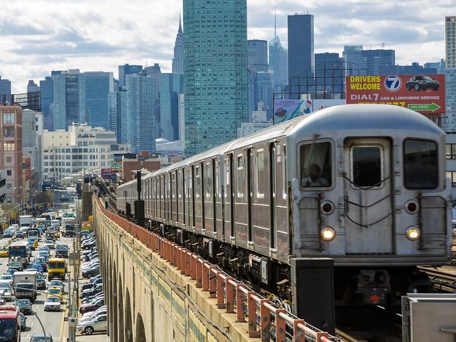 QUEENS, NEW YORK.  Train approaching  elevated subway station in Queens, New York. Finanancial buildings and New York skyline are seen in the background, on the left below can be seen a busy street full of cars at rush hour, cloudy, dramatic sky, horizontal orientation, USA