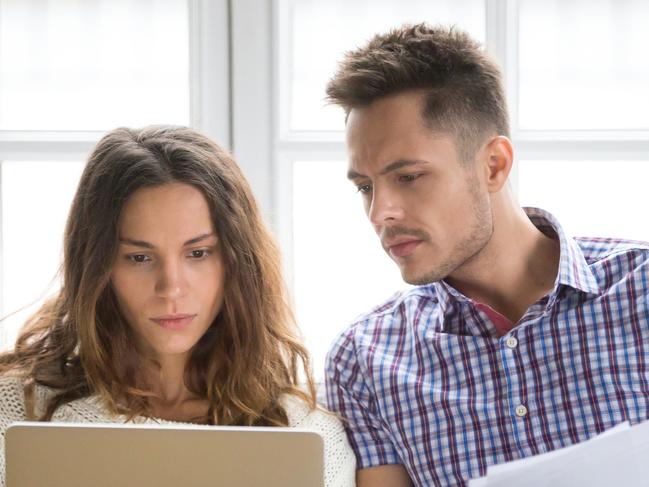 A couple discussing their household bills on the couch including their home loan. Picture: iStock.