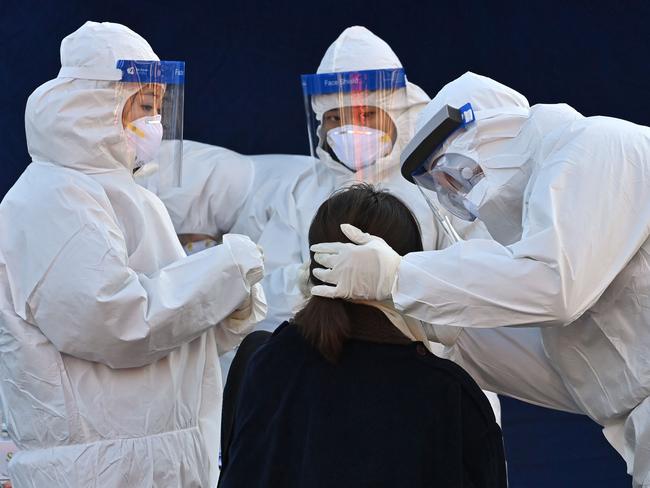 TOPSHOT - A medical staff member wearing protective gear takes a swab from a woman to test for the Covid-19 coronavirus at a temporary testing station outside Seoul station in Seoul on December 14, 2020. (Photo by Jung Yeon-je / AFP)