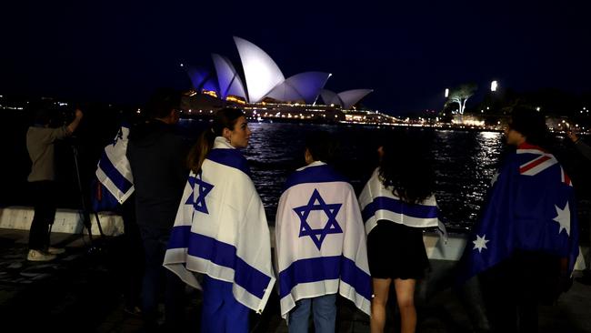 People wrapped in Israeli flags watch the Opera House illuminated in blue to show solidarity with Israel on October 9, 2023. Picture: AFP