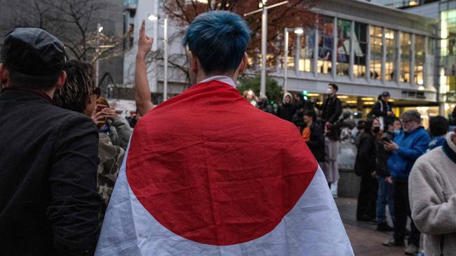 A man stands with the Japanese flag draped over his shoulders as fans celebrate after Japan's victory over Spain. Picture: AFP