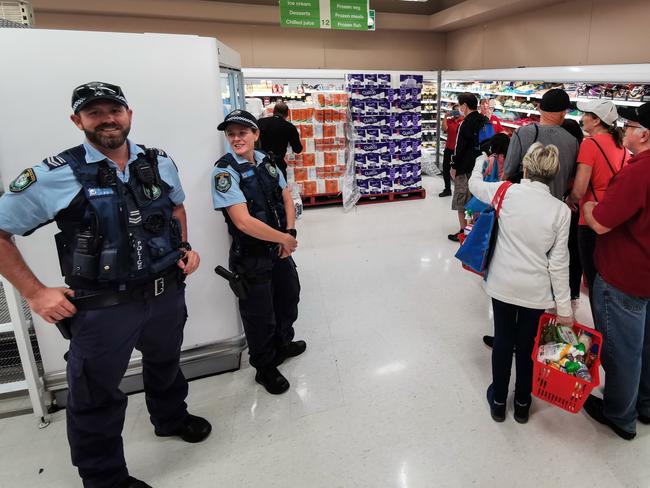 Police officers watch on as people queue for toilet paper, paper towel and pasta at a Coles Supermarket. Picture: AAP Image/James Gourley