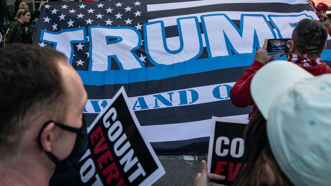 Donald Trump supporters display a large flag in front of people protesting in support of counting all votes in Pennsylvania. Picture: Chris McGrath/Getty Images/AFP