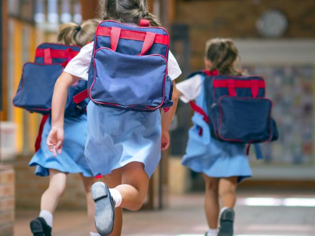 Rear view of excited students running towards entrance. Girls are carrying backpacks while leaving from school. Happy friends are wearing school uniforms. Source: iStock