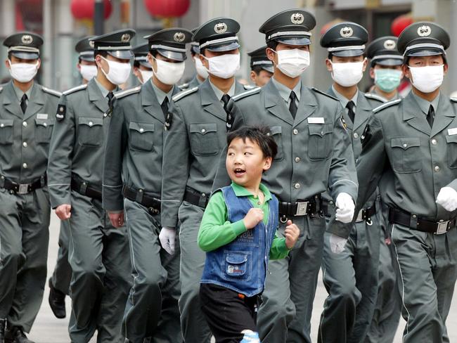 A young boy runs in front of a group of security guards wearing surgical masks to protect against the SARS virus as they patrol in Beijing, 2003. Picture: AP