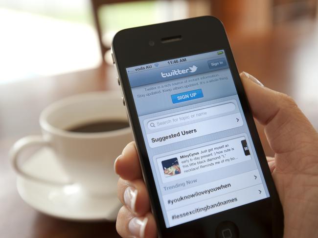 Female hand holding an iphone showing the Twitter sign up page. There is coffee on the dining table in the background. This image shows the iphone being used in a casual environment.