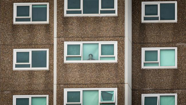 A lone woman is seen looking out the window of her apartment at the North Melbourne Public housing flats.