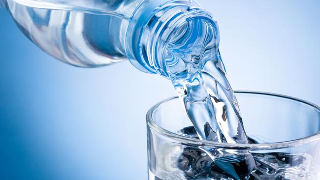 Pouring water from bottle into glass on blue background