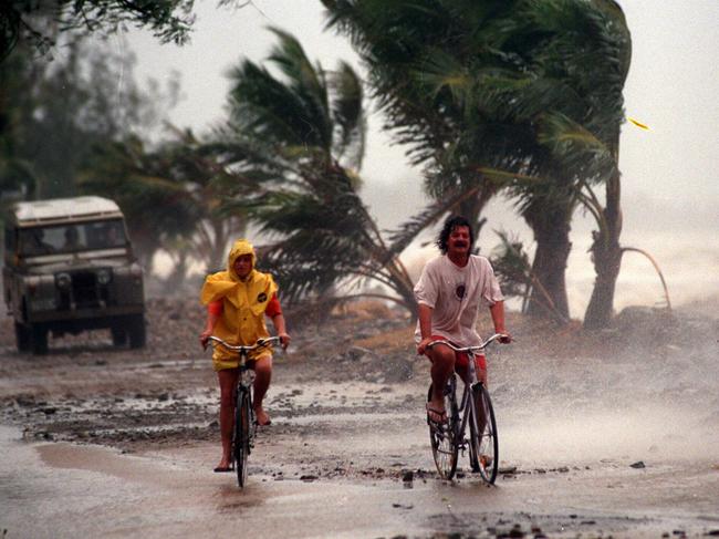 A couple cycle on the esplanade along Machans Beach near Cairns during high tide & strong winds, result of tropical cyclone Justin. Queensland / Weather