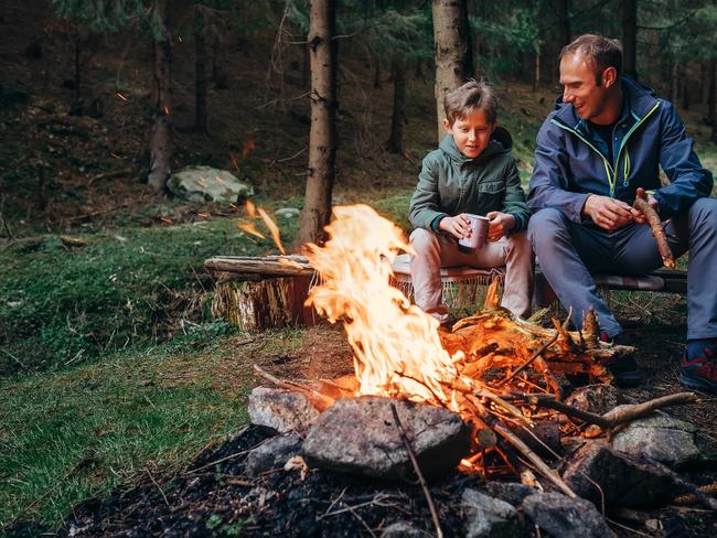 Father with son warm near campfire, drink tea and have conversation