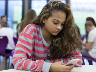 Female student sitting on her own at school. She has a smartphone in her hand and a stressed expression on her face. generic