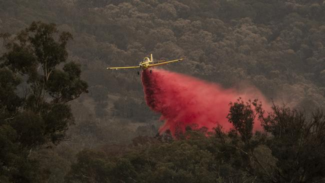 A small aircraft dumps fire retardant behind houses at the foot of Mount Tennant as the fire front in Orroral Valley creeps through the Namadgi National Park in January. Picture: Getty Images