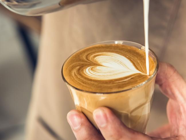 Professional barista holding coffee cup making beautiful heart shape latte art