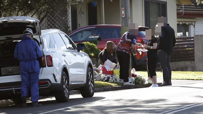 Family members and detectives visiting the floral tributes opposite the home where three children were killed in a suspicious fire. Picture: Richard Dobson