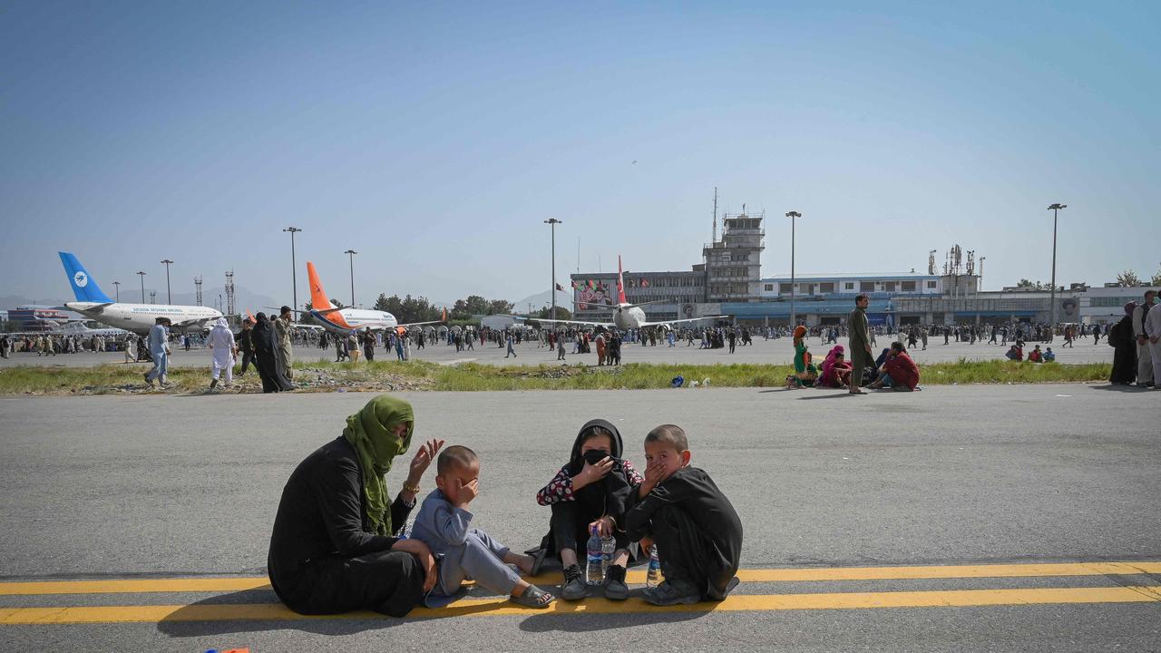 Afghan people sit along the tarmac as they wait to leave the Kabul airport on August 16. Picture: AFP