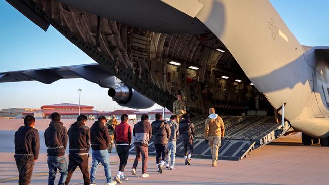 Nine restrained young men are led to a military plane as the military watch on. Picture: Posted on X by White House press secretary Karoline Leavitt