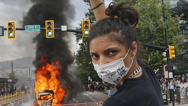 A protester looks on as a flipped over police vehicle burns in Salt Lake City.