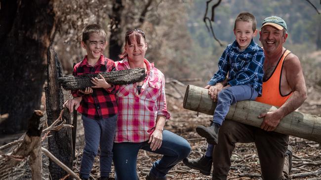 Colleen and Russell Foster with their twin 7-year-old sons, Jayden (red) and Rhys (blue), on their Omeo farm as the rebuild begins after a fire razed 600 acres of their land, a shed, fencing and machinery. Picture: Jason Edwards