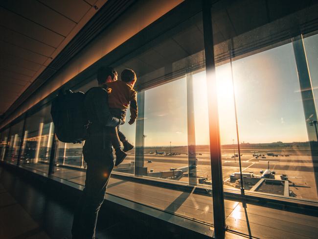 Young man and his son looking out of the window while waiting at an airport.