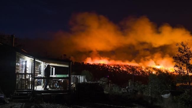 A resident watches from the deck of his shack as firefighters conducting a controlled burn along a ridge line at Miena. Picture: HEATH HOLDEN