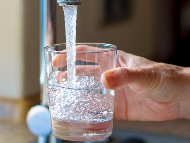 Woman filling a glass of water from a stainless steel or chrome tap or faucet, close up on her hand and the glass with running water and air bubbles