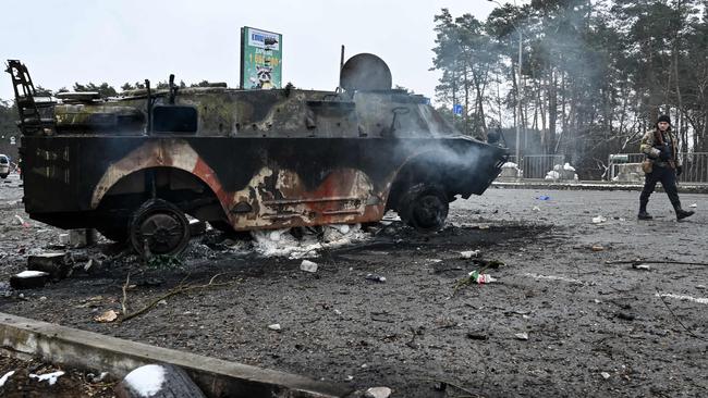 An armed man walks past a burned armoured personnel carrier (APC) BTR-4 on a check-point in the city of Brovary outside Kyiv on March 1. Picture: AFP