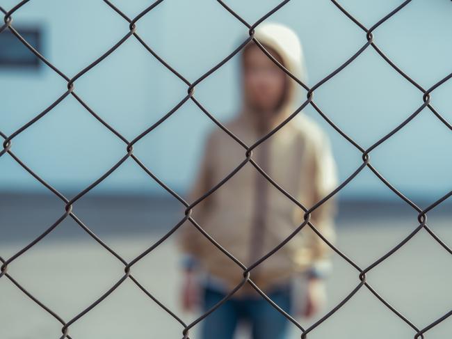 Sad boy standing behind grid fence