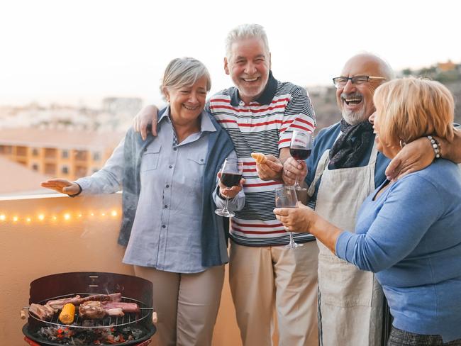 Happy senior friends having fun cheering with red wine at barbecue on terrace  - Mature people dining and laughing together at bbq party - Food drink and elderly friendship lifestyle concept