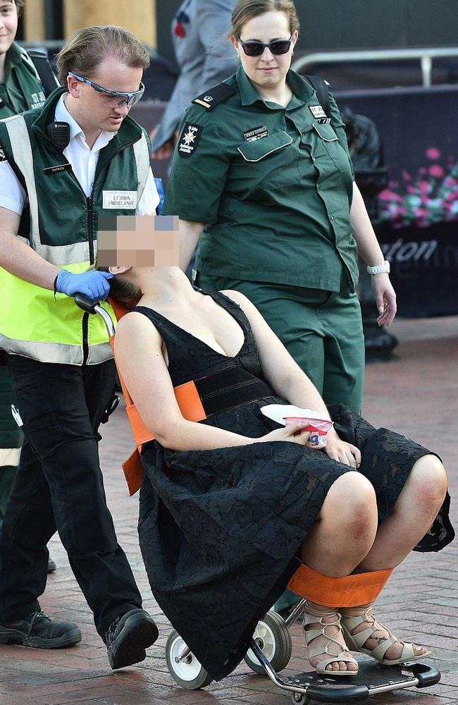 Strapped in with restraints on the special patient rescue chair, the woman still neatly dressed in a black frock is escorted from the field by St Johns Ambulance officers. Picture: AAP.