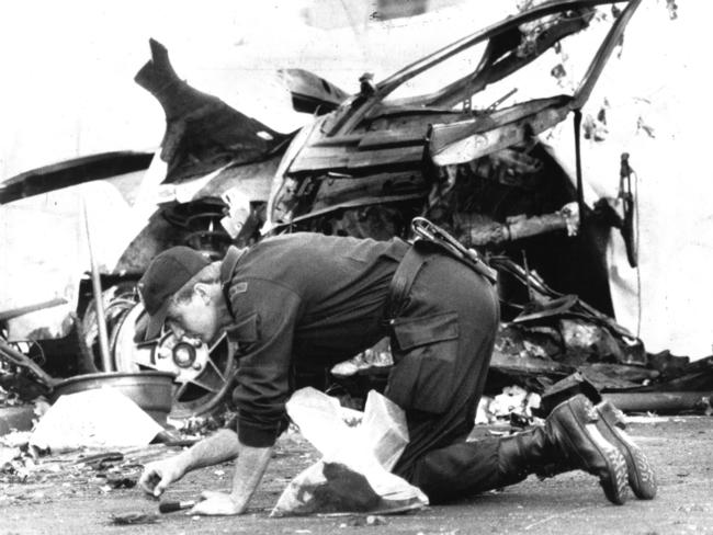 Armed with a brush and a plastic bag, an SOG officer sifts through the fragments around the mangled remains of the car which held the bomb. Picture: HWT library