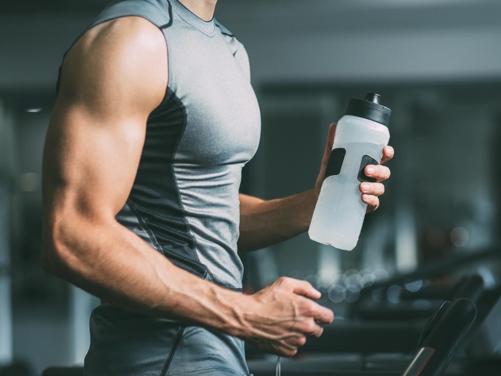 Man in sportswear running on treadmill at gym and holding bottle of water