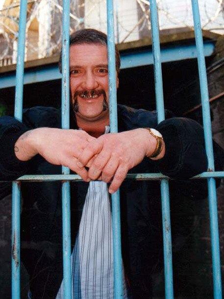 Reformed criminal Mark Chopper Read poses for photo behind bars during a visit to Pentridge Prison in Melbourne in 2002, where he was once an inmate. He died in 2013.