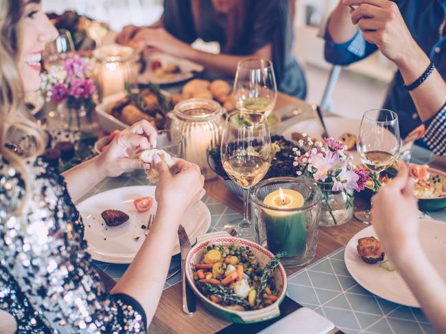 Friends having dinner party at home. It is a feast of food of all color and they are enjoy in every moment of the evening. They are happy and well dressed. Home is decorated with festive string lights and candles. Evening or night.