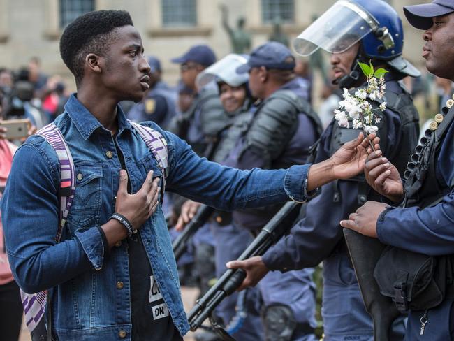 A student at the University of Witwatersrand offers flowers to South African anti-riot policemen during a running battle with the police forces on campus during a mass demonstration on October 4, 2016 in Johannesburg. Picture: AFP PHOTO / MARCO LONGARI
