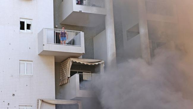 A woman stands on her balcony as smoke billows in the parking lot of a residential building following a rocket attack from the Gaza Strip in the southern Israeli city of Ashkelon. Picture: AFP