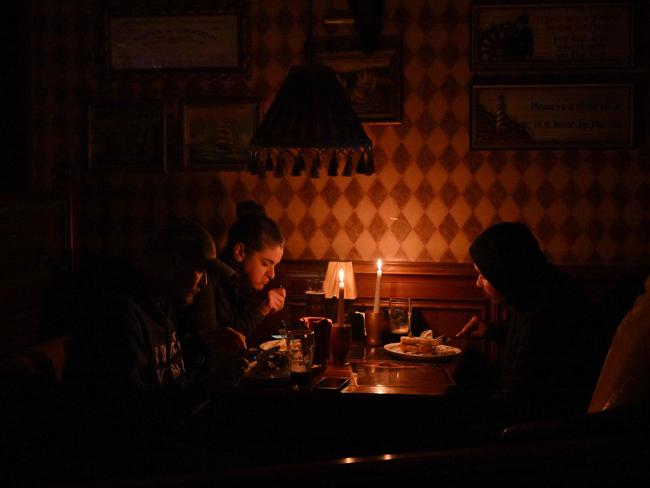 Ukrainians eating lunch by candlelight due to a power cut at a bar in Kyiv. The Ukrainian electrical system has been heavily affected by multiple Russian strikes. Picture: AFP